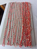 All 13 red glass seed bead necklaces laid out flat showing length and bead pattern