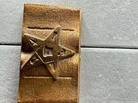 Front view of rectangular metal paperweight showing raised five-point star design
