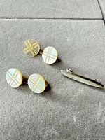 Pair of round cufflinks with cross motif and oval tie clip displayed on grey surface