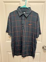 Front view of the charcoal Nike polo with red grid pattern and Swoosh logo