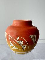 Rounded orange-yellow ceramic vase with white carved leaves