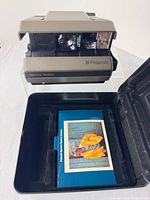 Camera folded open beside hard case and manual
