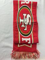 Folded scarf showing oval SF logo and fringed end