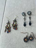 All three pairs laid out: multicolor chandelier, blue star drop, small round bronze dangle