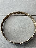 Full view of circular twisted sterling bangle on neutral background