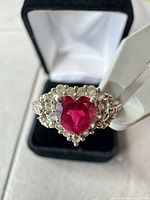 Close-up of ring showing heart-shaped red center stone and halo setting