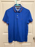 Front view of blue Tommy Hilfiger polo shirt on hanger.