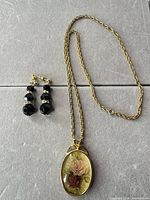 Necklace with floral pendant beside pair of black bead post earrings on flat surface