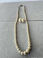 Full view of faux pearl necklace and matching earrings laid flat
