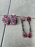 Both pairs of earrings displayed: rectangular clip-style with pink/aurora borealis rhinestones and floral pink rhinestone dangles