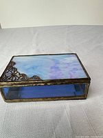 Closed stained glass jewelry box showing blue iridescent top panel, brass frame and side panel