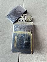 Front view of Zippo lighter, lid open showing engraving and wear