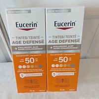 Front view of both boxed Eucerin Tinted Age Defense SPF 50 sunscreens 75 ml