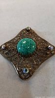 Front view of bronze filigree brooch showing green cabochon and AB crystals