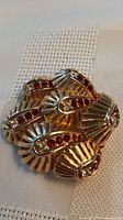 Front view of brooch showing fluted gold-tone segments and red/clear rhinestones