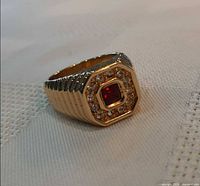 Ring angled view showing ruby-colour centre stone and clear crystal halo