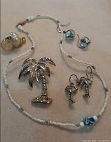 All jewellery pieces laid out: palm tree brooch, palm tree earrings, bead necklace, bead earrings, shell pendant
