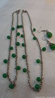 Two silver-tone bead necklaces and jadeite earrings laid on cloth
