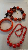 All three jewellery pieces laid out: bangle, orange/brown necklace, red-orange necklace