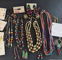 Full layout of necklaces, earrings and earring cards on black surface