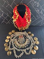 Overall lot showing red coin scarf on bust, silver-tone jewelry pieces arranged below, eight finger cymbals around perimeter