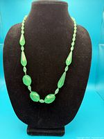 Single faceted green bead necklace displayed on black bust