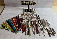 All timepieces and accessories laid out on white surface, showing quantity and variety of watches, pocket watches, straps, packaged bands, stand and tool