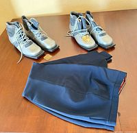Two pairs Alpina ski boots and folded navy pants displayed on table