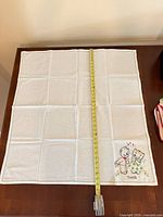 Square white cloth with kittens motif, tape measure showing size