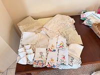 Group of lace table coverings, stacks of napkins, embroidered towels displayed on table