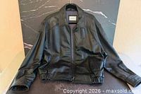 Front view of black leather jacket laid flat showing zipper front, pockets, collar, cuffs, waistband
