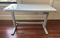 Front view of white glass top Tresanti adjustable desk on metal frame