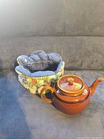 Teapot and tea cozy side by side on couch