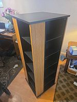 Full view of rotating media tower showing black shelves and oak-finish sides