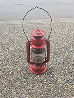Full view of red metal hurricane lantern standing upright