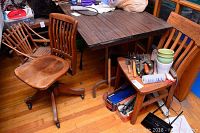 Photo of wood table, chairs, and a small table with tools, showing furniture condition and setting
