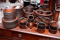 Wide view of stacked brown speckled plates, bowls and mugs on wooden table