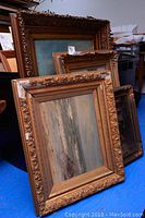 Four oil paintings stacked showing frames and visible damage