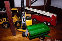Photo showing a Tonka metal tracked crane with white boom, green metal wagon, and red fire engine on hardwood floor.