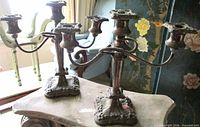 Front angled view of both silverplate candelabras displaying overall form and ornate bases