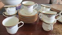 Stack of eight saucers surrounded by eight matching teacups displaying floral band and gold trim