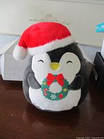 Front view of Squishmallows penguin plush with Santa hat and wreath
