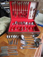 Open flatware box showing knives in lid, forks and spoons in case, loose utensils in front