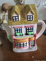Front view of cottage-style teapot showing shop facade and spout
