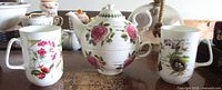 Group view of Portmeirion personal teapot with cup stacked and two Rose of England mugs