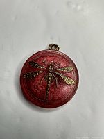 Front view showing red round pendant with brass dragonfly design