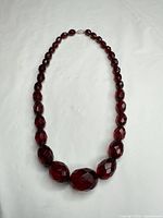 Full view of graduated deep red faceted glass bead necklace laid flat