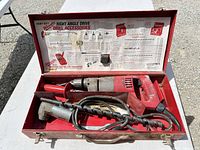 Open metal case showing drill, attachment, handle, bit, interior label