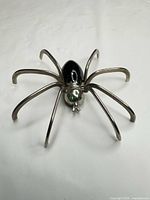 Front view of silver-tone spider brooch showing black enamel body and green rhinestone eyes