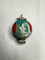 Front view of round pendant showing turquoise and red inlay with silver symbol